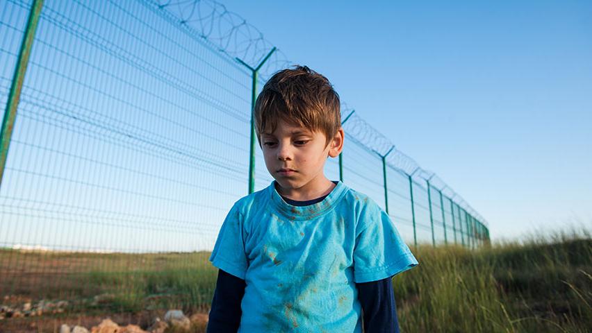 Boy refugee walking along fence